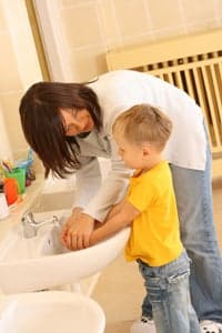Woman helps preschooler wash hands